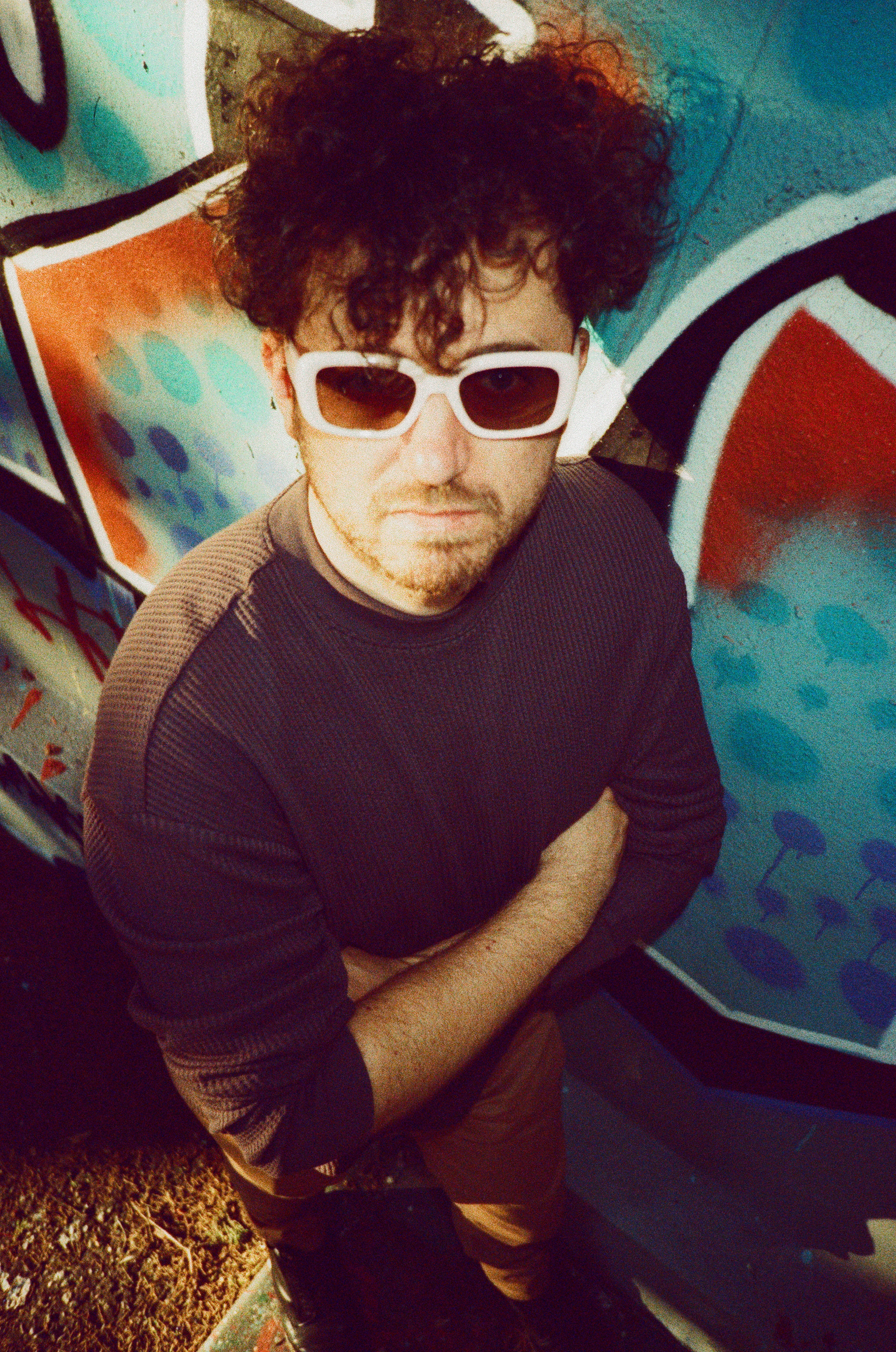 Overhead portrait of Kevin Stefanescu wearing white sunglasses against a painted wall